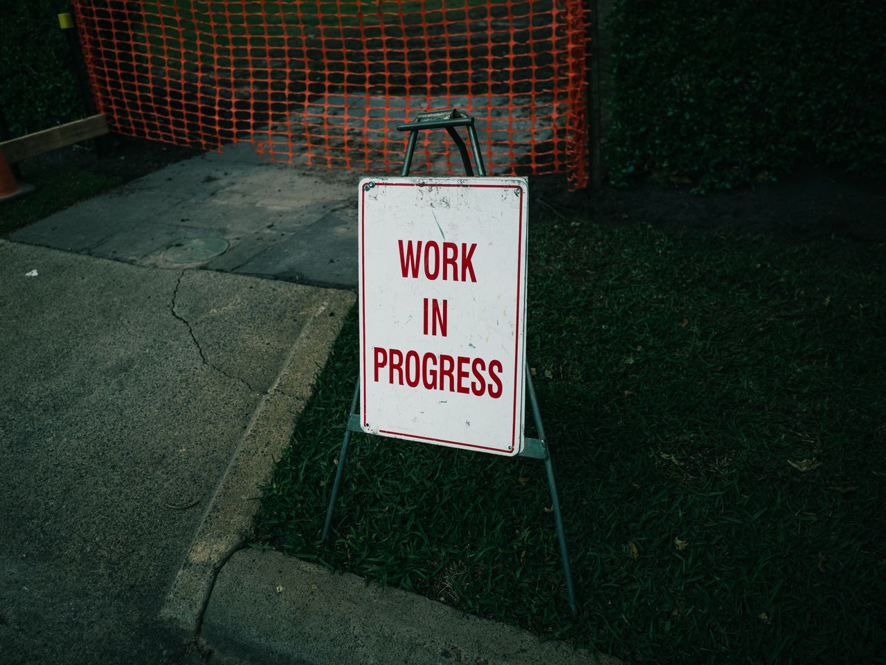 services-01 A 'Work in Progress' sign stands on a sidewalk next to safety barriers.