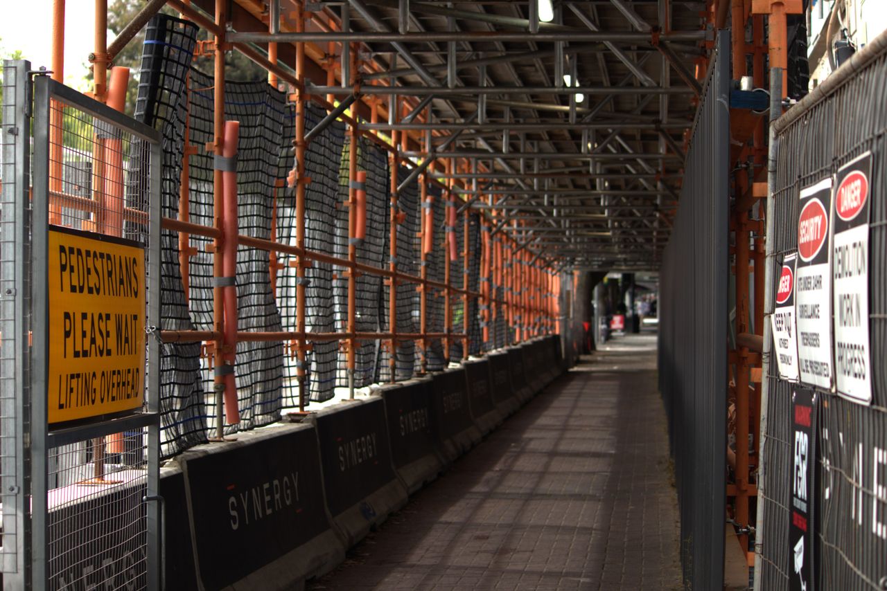 services-02 Pedestrian walkway through a construction site with safety signs and scaffolding overhead.